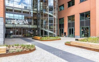 Entree van het moderne kantoorpand op Kabelweg 57, Amsterdam Sloterdijk, met glazen gevel en zitplekken buiten. Perfecte locatie voor bedrijven die kantoorruimte willen huren.