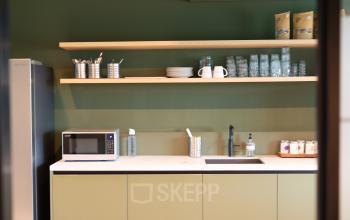 Kantine met groene kasten en open houten planken met servies en glazen op Kabelweg 37, Amsterdam Sloterdijk, geschikt voor gebruik door kantoormedewerkers.