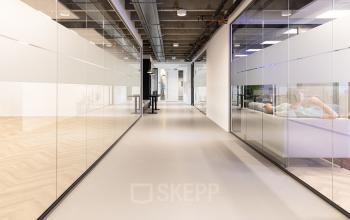 Moderne kantoorruimte huren aan de Kabelweg 37 in Amsterdam Sloterdijk, met glazen wanden, afgewerkt plafond, en een stijlvolle lange gang. Een persoon ontspannen in een lounge ruimte.