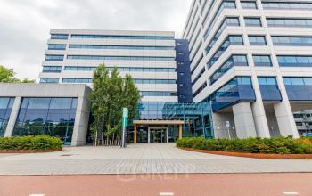 Moderne kantoorpand bij Kabelweg 37, Amsterdam Sloterdijk met glazen entree en omringd door groen, ideaal voor wie kantoorruimte wil huren.