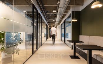 Kantoorruimte huren aan de Kabelweg 37 in Amsterdam Sloterdijk, met moderne inrichting. Glazen wanden, industriële afwerking en een persoon die door de gang loopt. Ideaal voor bedrijven die kantoren zoeken.