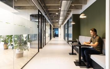 Modern kantoorpand op Kabelweg 37 in Amsterdam Sloterdijk met glazen wanden en loungegedeelte. Persoon werkt op laptop aan tafel. Ideaal voor kantoorruimte huren.