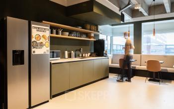 Kantoorpand op Kabelweg 37 in Amsterdam Sloterdijk met gemeubileerde pantry. Een persoon geniet van een koffiepauze in een moderne kantoorsetting. Ideale plek voor kantoorruimte huren met alle voorzieningen.
