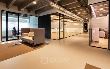 Moderne kantoorruimte huren in een open vloerplan bij Kabelweg 37, Amsterdam Sloterdijk. Glazen wanden, houten vloer en comfortabele zitgelegenheden creëren een uitnodigende werkruimte.
