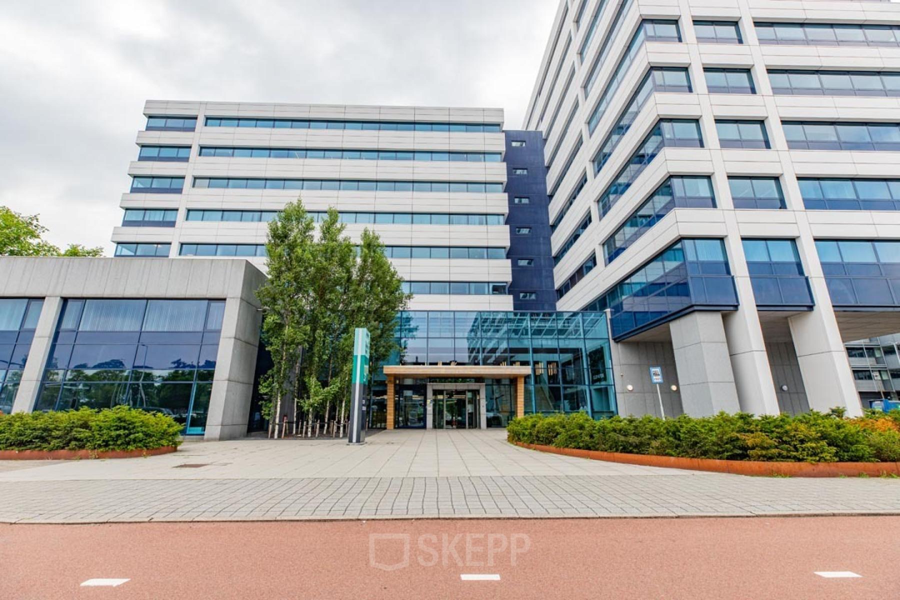 Moderne kantoorpand bij Kabelweg 37, Amsterdam Sloterdijk met glazen entree en omringd door groen, ideaal voor wie kantoorruimte wil huren.