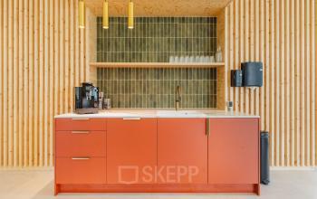 Moderne pantry met rode kasten en houten accenten in kantoorpand aan de Basisweg 32, Amsterdam Sloterdijk. Voorzien van een koffiezetapparaat en glazen, ideaal voor pauzemomenten tijdens het kantoorruimte huren.