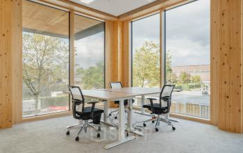 Moderne kantoorruimte huren met grote ramen en houten wanden op Basisweg 32 in Amsterdam Sloterdijk, zonder mensen aanwezig, met drie stoelen rond een tafel.