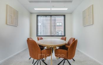 Moderne vergaderruimte met zes comfortabele stoelen en een ronde tafel, ideaal voor zakelijke bijeenkomsten in een kantoorpand op Basisweg 32 in Amsterdam Sloterdijk.