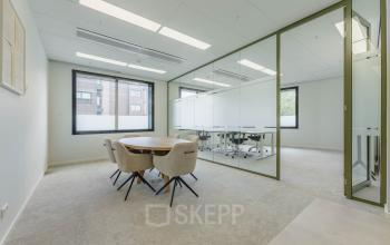 Vergaderruimte in kantoorpand op Basisweg 32, Amsterdam Sloterdijk met lichte muren, raam en ronde tafel. Ideaal om een kantoorruimte te huren voor zakelijke bijeenkomsten.