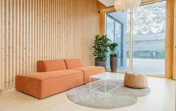 Moderne entree van kantoorpand aan Basisweg 30, Amsterdam Sloterdijk met houten panelen, oranje bank en grote ramen. Ruimte voor interactie voordat je over kantoorruimte huren nadenkt.