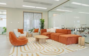 Stijlvolle kantoorruimte huren in Amsterdam Sloterdijk, met moderne oranje en witte loungezitjes en een houten tafel op Basisweg 32. Glazen wanden scheiden vergaderruimtes.