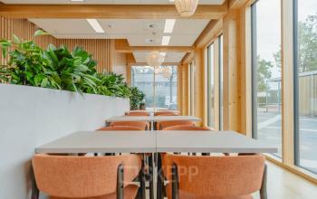 Moderne kantoorruimte met veel natuurlijk licht aan Basisweg 32, Amsterdam Sloterdijk. Gezellige ruimte met tafels en stoelen, geschikt voor vergaderingen of informele werkplekken, met uitzicht op de stad.