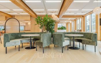 Moderne kantoorruimte huren in Amsterdam Sloterdijk met groene banken en tafels, natuurlijke materialen en veel lichtinval. Ideale plek voor informeel overleg of samenwerking.