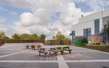 Exterieur van kantoorpand aan de Basisweg 32, Amsterdam Sloterdijk met terras en kleurrijke picknicktafels, ideaal voor huur als ontspanningsruimte voor werknemers.