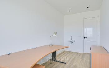 Zicht op een minimalistisch kantoor in Amsterdam Sloterdijk met een houten bureau, bureaulamp en wastafel, ideaal voor wie kantoorruimte wil huren.