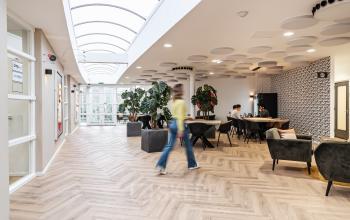 Moderne kantoorpand met open ruimte aan Arlandaweg 92, in Amsterdam Sloterdijk. Medewerkers aan het werk aan tafels en ontspannen in comfortabele zitjes.