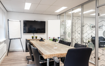 Vergaderruimte in kantoorpand op Arlandaweg 92, Amsterdam Sloterdijk, met houten tafel, zwarte stoelen, flip-over en groot digitaal scherm.