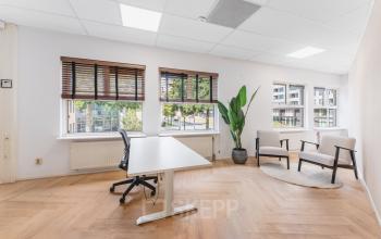 Verlichte kantoorruimte te huur aan de Arlandaweg 92, Amsterdam Sloterdijk met houten vloer, groot bureau en vensterplanten. Ideaal voor werk of vergaderingen met uitzicht op de stad.