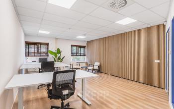 Lichte kantoorruimte huren op Arlandaweg 92, Amsterdam Sloterdijk. Het kantoorpand heeft een moderne houten wand en houten vloer, met verstelbare bureaus en stoelen, ideaal voor creatieve werkplekken.