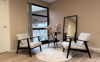 Kantoorinterieur op Arlandaweg 92, Amsterdam Sloterdijk, met een stijlvolle zithoek met twee stoelen, een rond kleed, en een bijzettafel. Grote ramen zorgen voor veel natuurlijk licht.