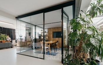 Modern ingerichte kantoorruimte op Overtoom 141 met glazen scheidingswanden en groene planten, collega's aan het werk op de achtergrond.