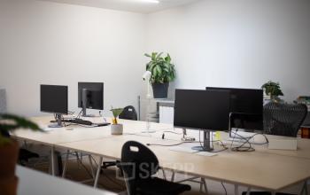 Ruime kantoorruimte met meerdere bureaus en computerschermen, veel licht en een plant in de hoek; ideaal om te huren in Amsterdam West.