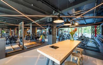 Moderne kantoorruimte huren in een kantoorpand op Nachtwachtlaan 20, Amsterdam West met een grote open ruimte, overal fitnessapparatuur en een centrale tafel met krukken.