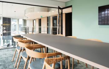 Kantoorruimte huren aan Overschiestraat 63 in Amsterdam Nieuw-West, met een lange tafel, houten stoelen en een moderne inrichting. Ruimte is geschikt voor vergaderingen of conferenties.