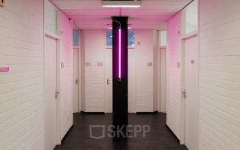 Lichte hal van kantoorpand op Rigakade 10, Amsterdam West met witte muren en een opvallende roze verlichtingsbalk in het midden. De gangen leiden naar diverse kantoorruimte. Perfect voor kantoor huren in Amsterdam.