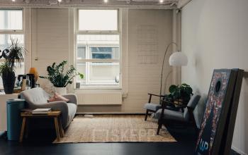 Stijlvolle kantoorruimte huren op Rigakade 10, Amsterdam West, met een moderne inrichting inclusief comfortabele zitplaatsen, planten en voldoende natuurlijk licht.