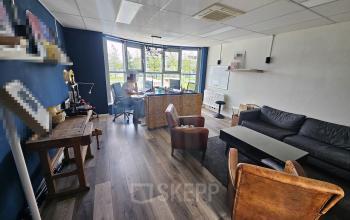 Kantoorruimte huren op Gyroscoopweg 23-25, Amsterdam Westpoort. Ruime, gemeubileerde kantoorruimte met moderne inrichting en grote ramen, een persoon aan het werk.