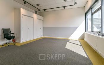 Lichte kantoorruimte in Amsterdam Westpoort met grote ramen, kantoorpand Poortland 242, Amsterdam. Lege ruimte met tapijtvloer en een enkele bureaustoel, ideaal voor toekomstige inrichting.