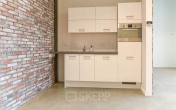 Kantoorruimte huren in Amsterdam Westpoort met moderne keuken, witte kasten en bakstenen muur, geschikt voor huur als pantry.