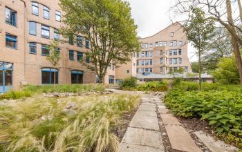 Buitenzijde van een kantoorpand aan Bijlmerplein 888 in Amsterdam Zuid-Oost, omgeven door een groene tuin met een wandelpad.