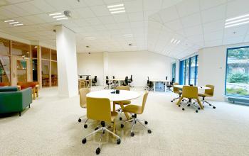 Lichte kantoorruimte huren in Amsterdam Zuid-Oost met verschillende werkplekken en moderne inrichting. Grote ramen voor natuurlijk lichtinval en meerdere tafels met stoelen aanwezig.