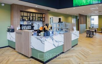 Moderne receptie met marmeren balie in kantoorpand Hogehilweg 24, Amsterdam Zuid-Oost. De ruimte heeft houten vloeren en groen-witte muren, geschikt voor kantoorruimte huren, met zitgedeeltes en ontvangstmogelijkheden.