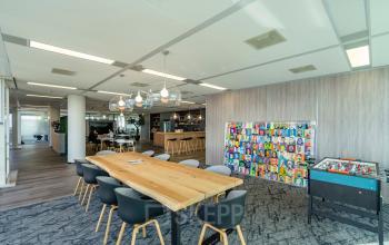 Modern kantoorpand in Amsterdam Zuid-Oost met ruime open vloerindeling, voorzien van een lange houten tafel en speels ingerichte zithoek.
