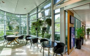 Moderne kantoorruimte in Amsterdam Zuid-Oost met glazen wanden en stijlvolle meubels. Veel natuurlijk licht met groene accenten en rond tafels voor informele bijeenkomsten. Belangrijke locatie voor kantoorruimte huren.