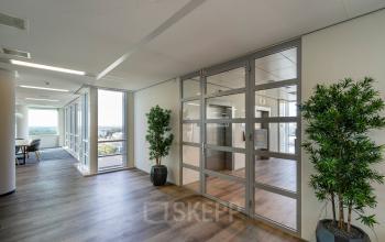 Moderne kantoorruimte in Amsterdam Zuid-Oost met glazen wanden en houten vloer, geschikt voor kantoorruimte huren. Groene planten decoreren de lichte en open werkruimte.