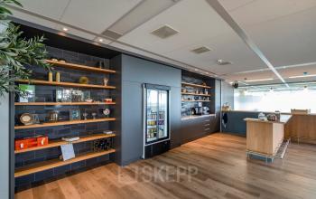 Modern ingerichte pantry in een kantoorpand op De Entree 230-266 in Amsterdam Zuid-Oost, voorzien van houten planken met decoratieve items en een koelkast.