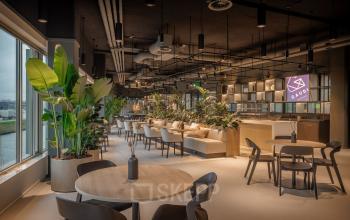 Moderne, gemeubileerde kantoorruimte aan de Herikerbergweg 288 in Amsterdam Zuid-Oost met open werkplekken, tafels, stoelen en veel groen. Ideaal voor bedrijven die kantoorruimte willen huren.