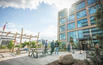 Moderne kantooromgeving aan de Luttenbergweg 8, Amsterdam Zuid-Oost, met mensen die zakelijk overleggen bij picknicktafels buitenshuis voor een ruim en uitnodigend kantoorpand.