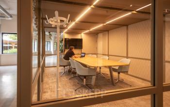 Vergaderruimte in kantoorpand op Luttenbergweg 8, Amsterdam Zuid-Oost, met persoon bezig op laptop aan grote tafel onder stijlvolle verlichting. Ruimte te huur voor zakelijke bijeenkomsten.