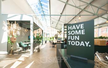 Lichte en moderne kantoorruimte te huur op Luttenbergweg 8 in Amsterdam Zuid-Oost, met glazen dak en groene accenten. Ideaal voor creatieve werkplekken in een aantrekkelijk kantoorpand.