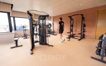 Goed uitgeruste fitnessruimte in kantoorpand op Luttenbergweg 8, Amsterdam Zuid-Oost met diverse apparaten en een persoon die sportieve activiteiten uitvoert.