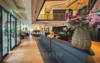 Kantoorruimte te huur in Amsterdam Zuid-Oost met modern interieur op Luttenbergweg 8. Mensen voeren zakelijke activiteiten uit in een gemeubileerde ruimte met bloemen en moderne meubels.