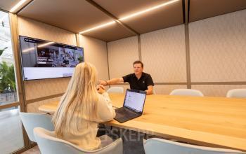 Vergaderruimte in kantoorpand aan de Luttenbergweg 8, Amsterdam Zuid-Oost met twee personen in overleg. Moderne inrichting met grote houten tafel en beeldscherm aan de muur, ideaal voor kantoorruimte huren.