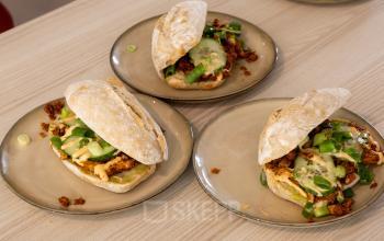 Houten tafel in een kantoorruimte met drie borden broodjes, ideaal voor een lunchpauze. Het kantoorpand op Luttenbergweg 8 in Amsterdam Zuid-Oost biedt verhuurmogelijkheden voor werkruimtes.