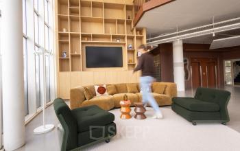 Moderne, gemeubileerde lounge in een kantoorpand aan Luttenbergweg 8, Amsterdam Zuid-Oost, met comfortabele zitplaatsen en een wandmeubel. Een persoon loopt door de ruimte.