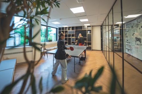 Kantoorruimte op Luttenbergweg 8 met glazen wanden, houten vloer, en personeelsleden die tafeltennis spelen, ideaal voor zakelijke huur in Amsterdam Zuid-Oost.
